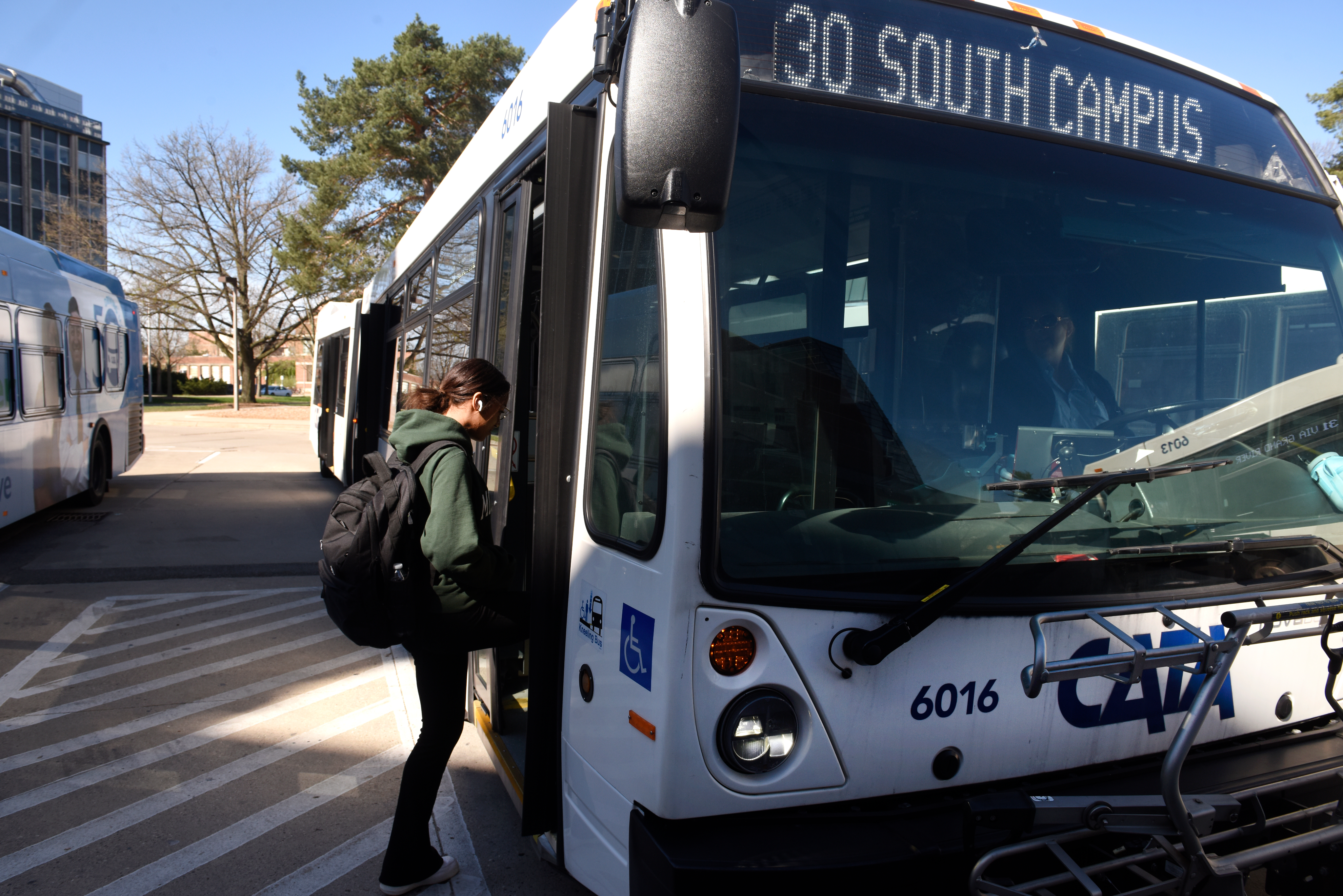 Passenger with a backpack boarding CATA Route 30 South Campus bus at a bus stop