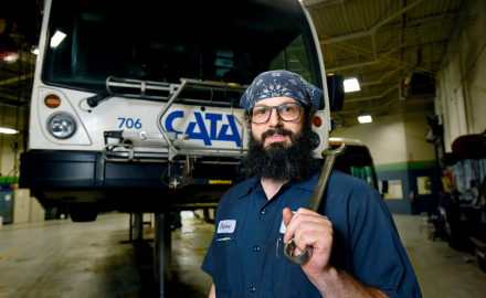 CATA mechanic holding tool in front of a lifted CATA bus