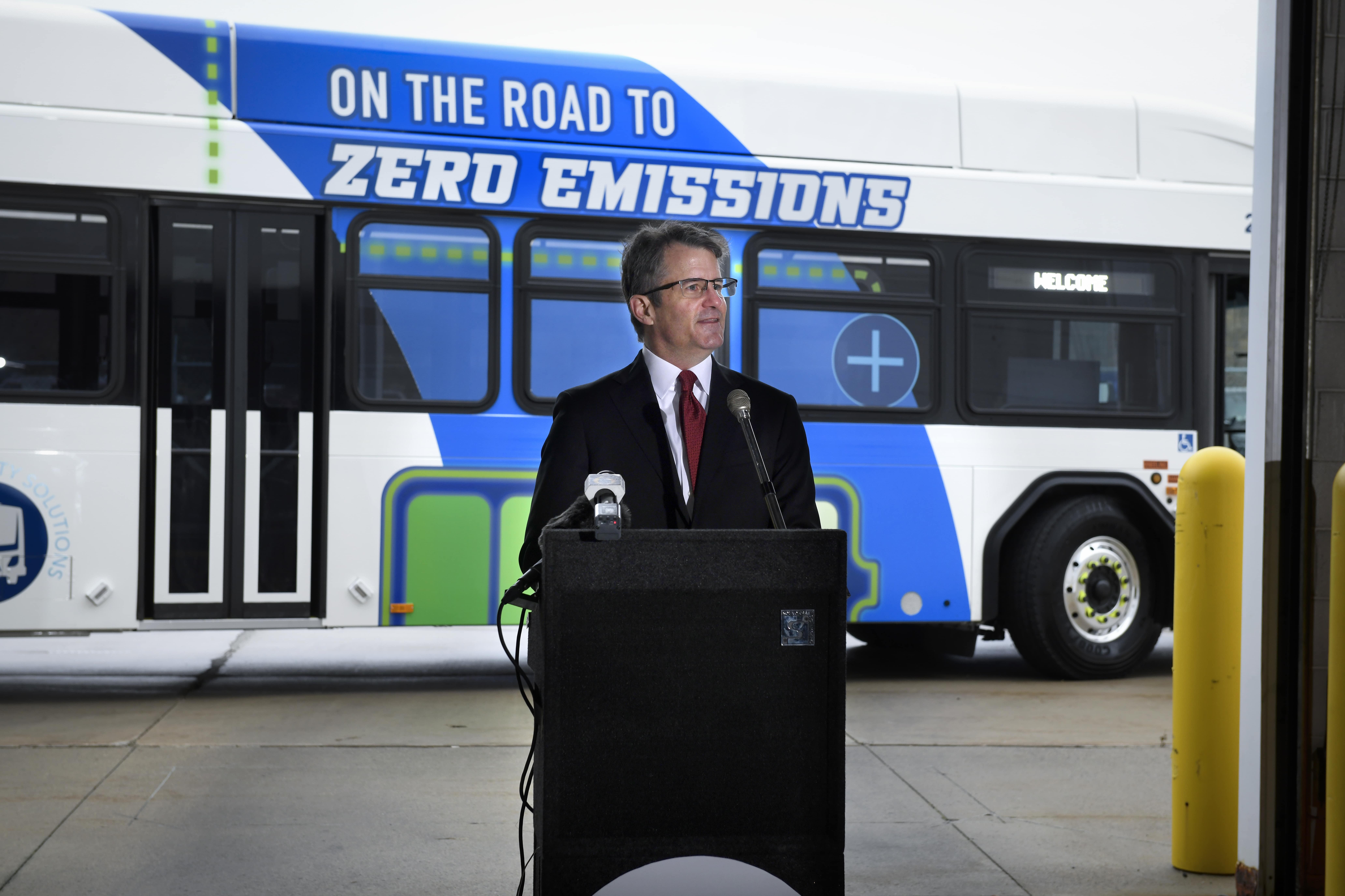 CATA's CEO, Bradley T. Funkhouser, speaking at a podium in front of the electric bus