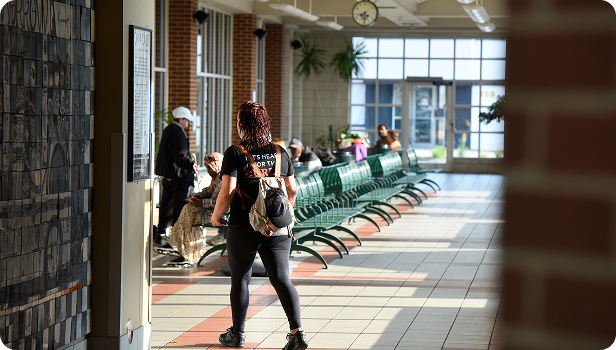 Bus terminal waiting area with green benches and a person walking toward windows