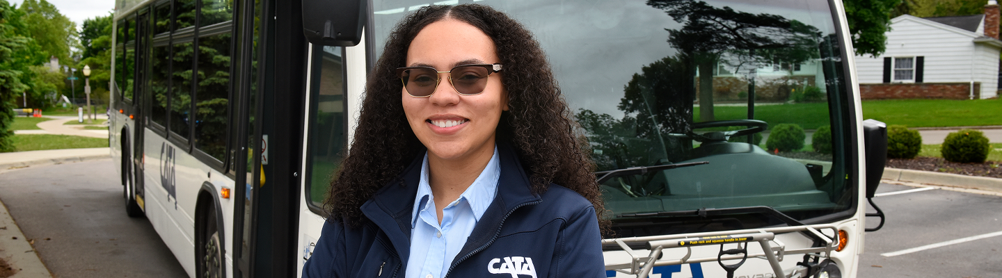 Smiling bus driver standing in front of a city bus outdoors.
