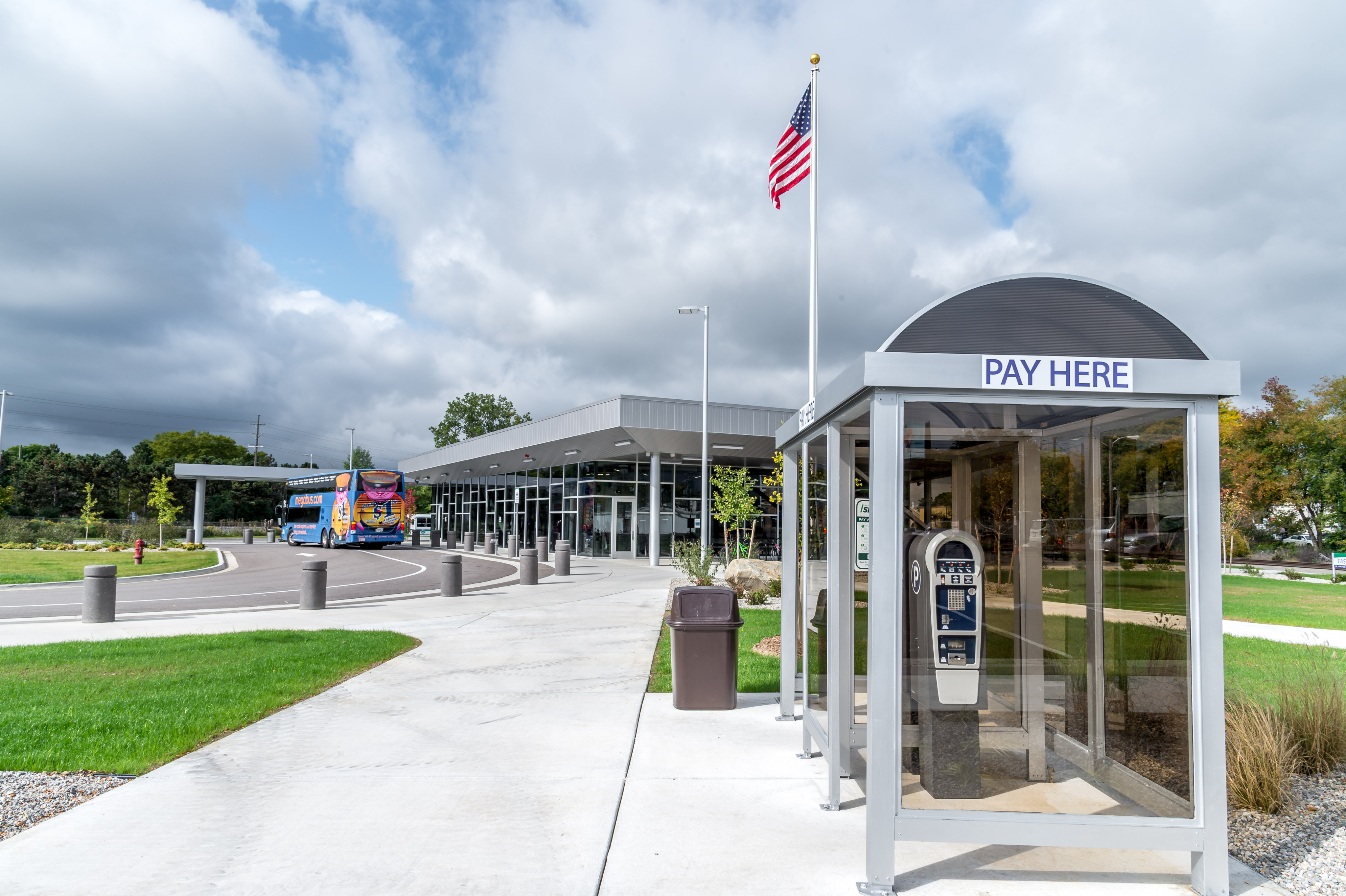 Bus station entrance with a ‘Pay Here’ kiosk and a bus parked near the building.