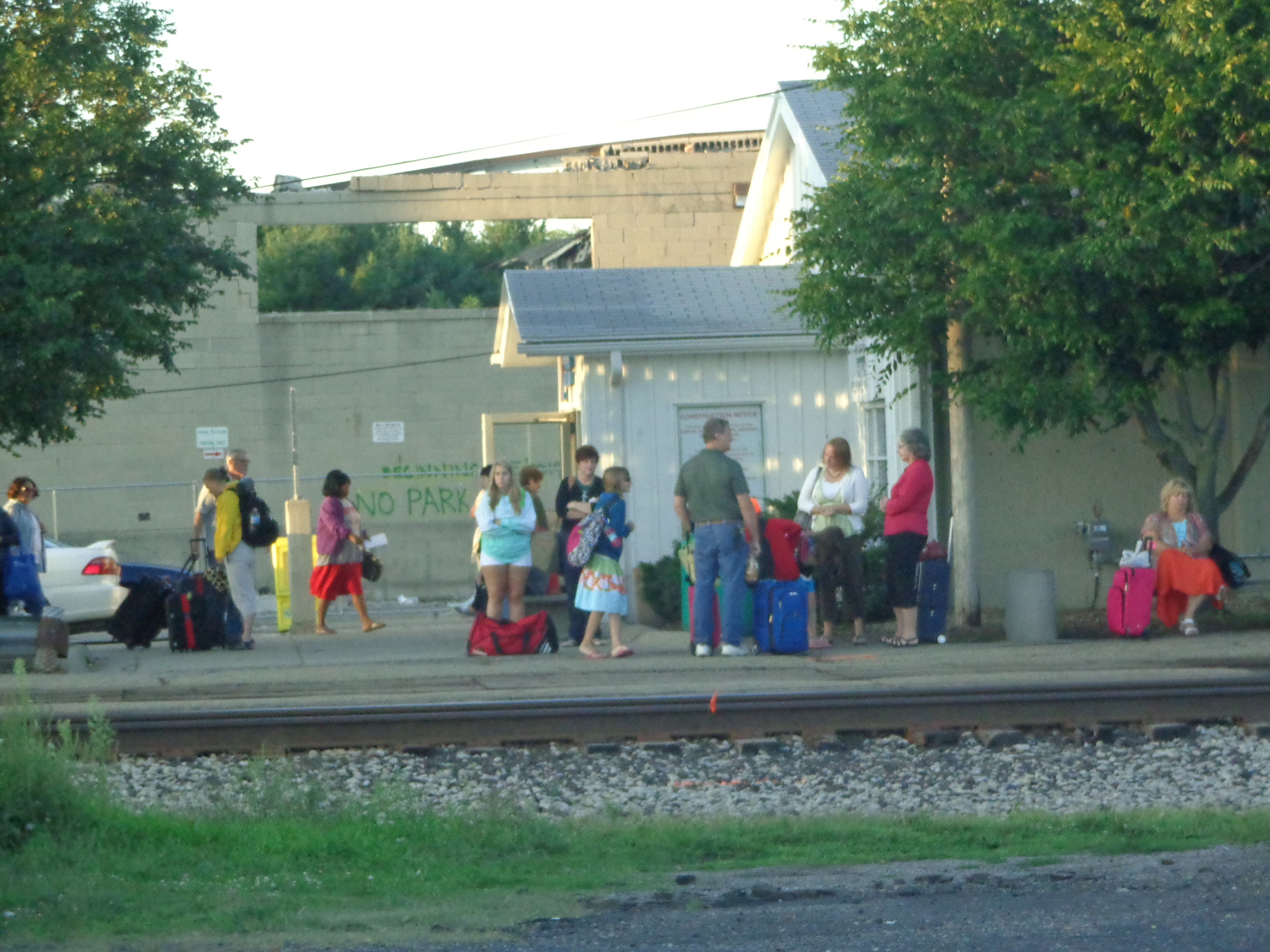 People wait for the train next to a white train station building in the early morning