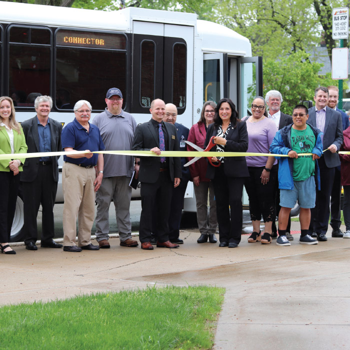 A group of people standing in front of a CATA spec-tran vehicle holding a ribbon. A woman with ceremonial scissors is poised to cut the ribbon.