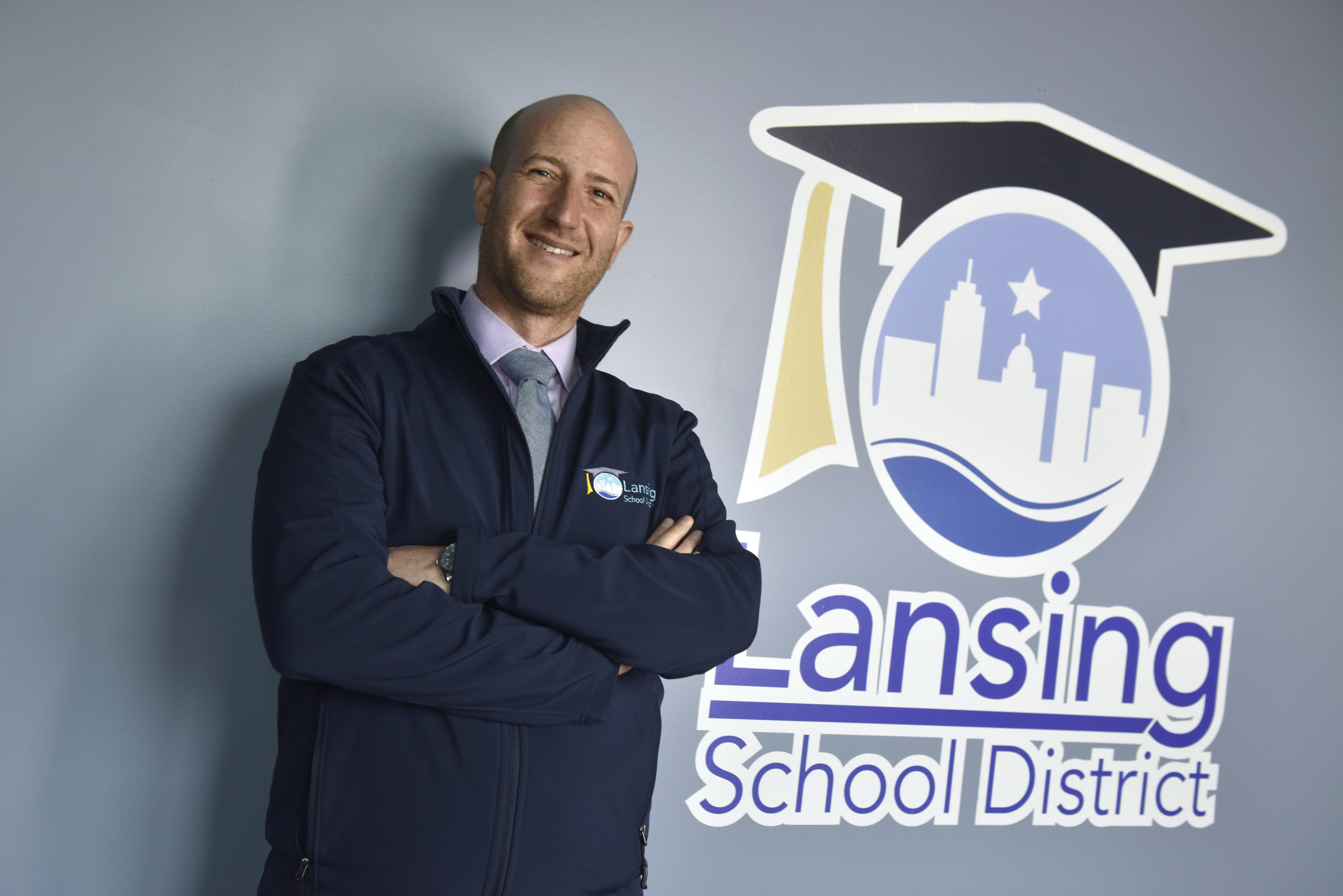 Ben Shuldiner stands in front of the Lansing school district sign