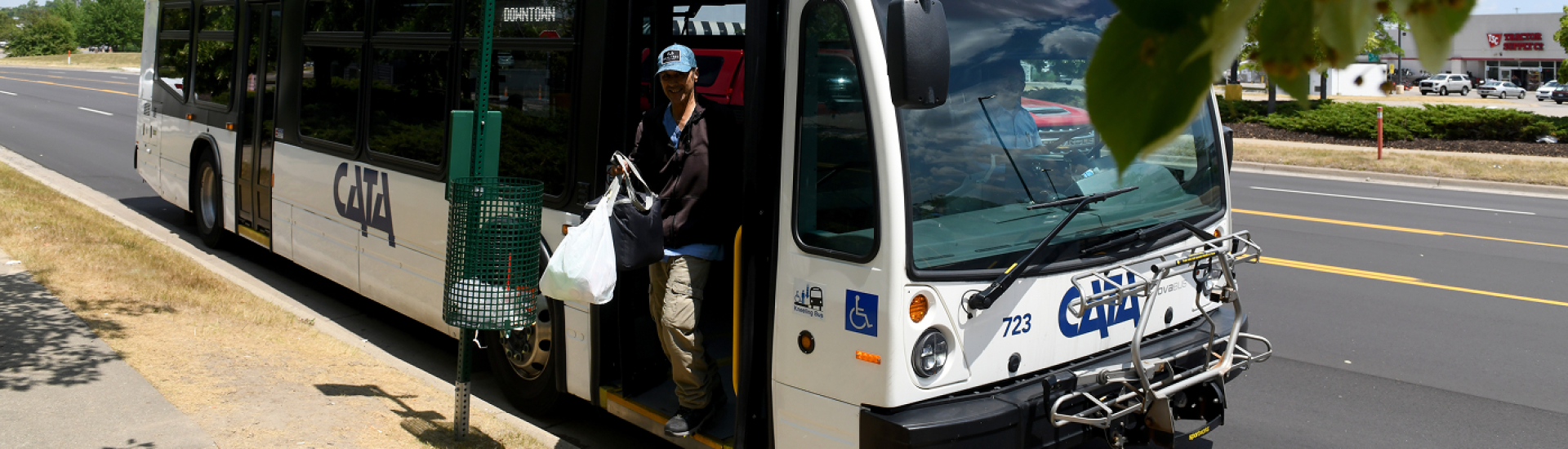 Person getting off a CATA city bus at a roadside bus stop carrying shopping bags.