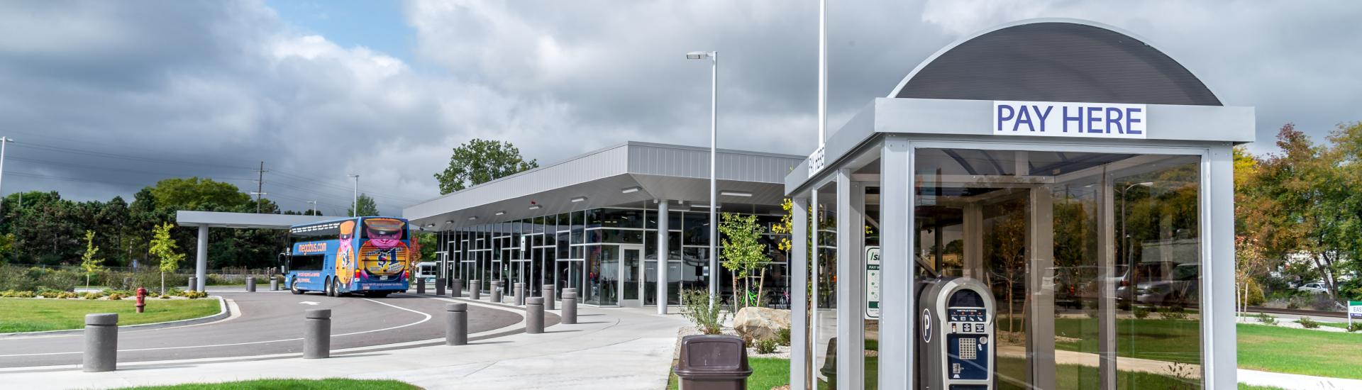 Bus station entrance with a ‘Pay Here’ kiosk and a bus parked near the building.