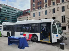 A white CATA bus parked on a city street next to a blue promotional table and red folding chairs.”.  • Ride with our apps: “A woman sitting on a bus, using her smartphone to access a transit app while holding a bus pass.”
