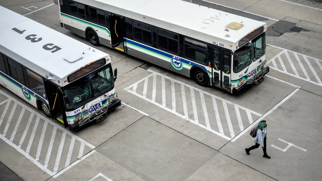 “Aerial view of two white CATA buses parked in designated stalls while a pedestrian walks nearby on the pavement.